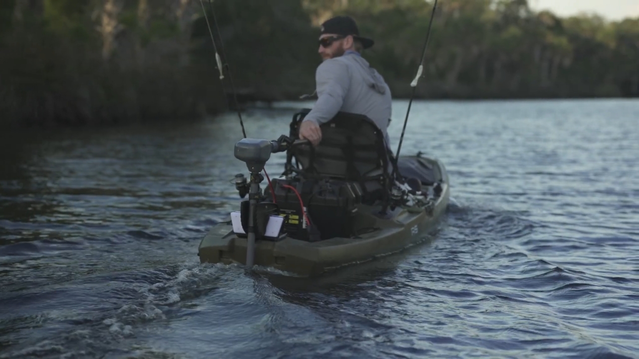 Man steering a fishing kayak with a rear-mounted trolling motor on calm water