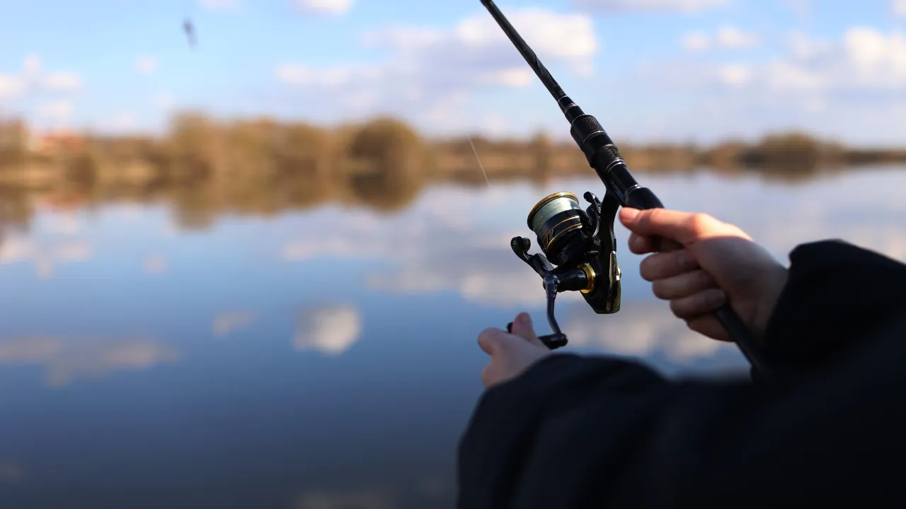 Angler holds a spinning reel over a calm lake