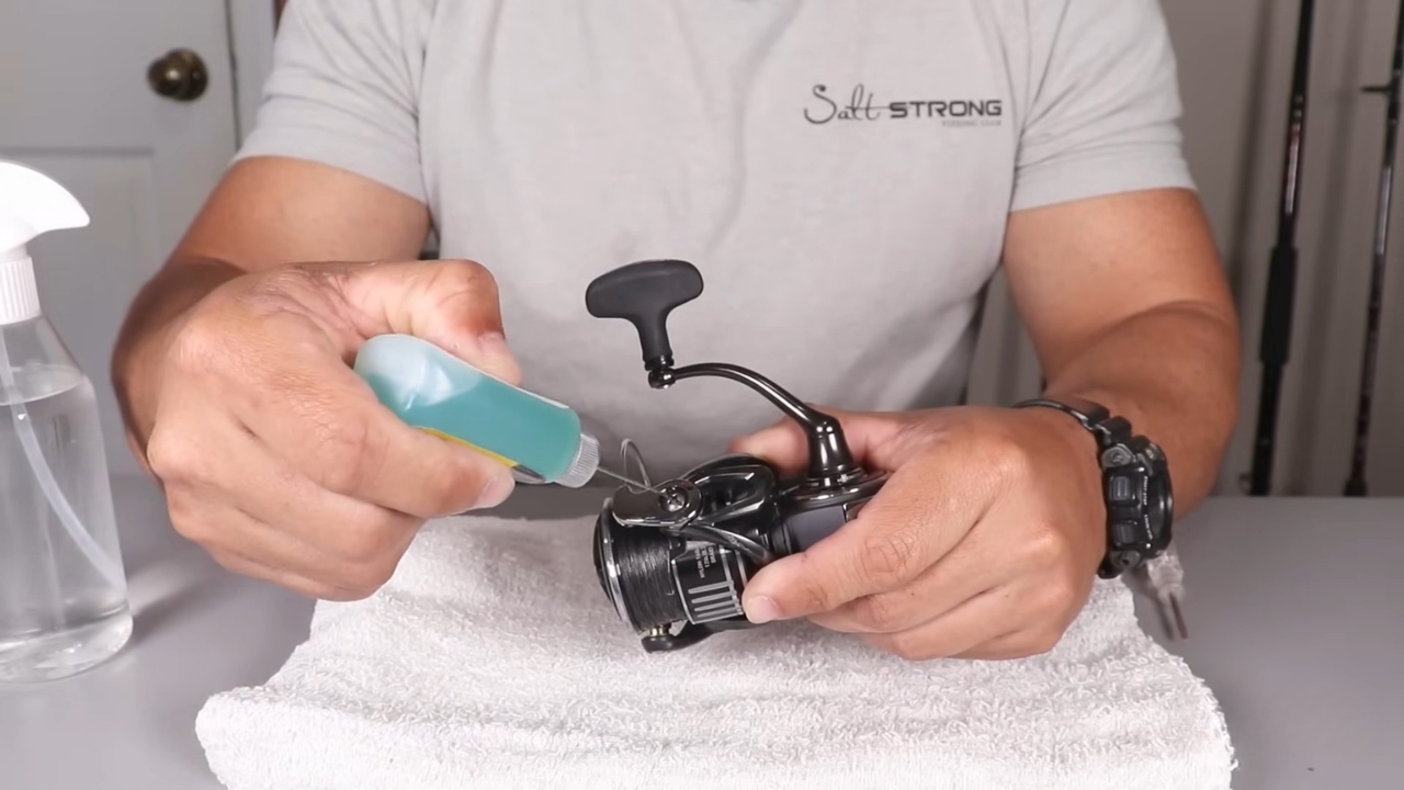 Person adds oil to a fishing reel during routine maintenance