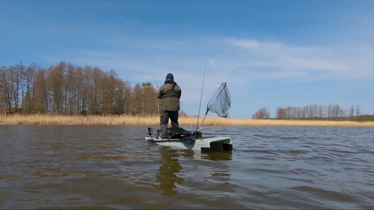 Angler standing on a motorized fishing kayak in calm lake water