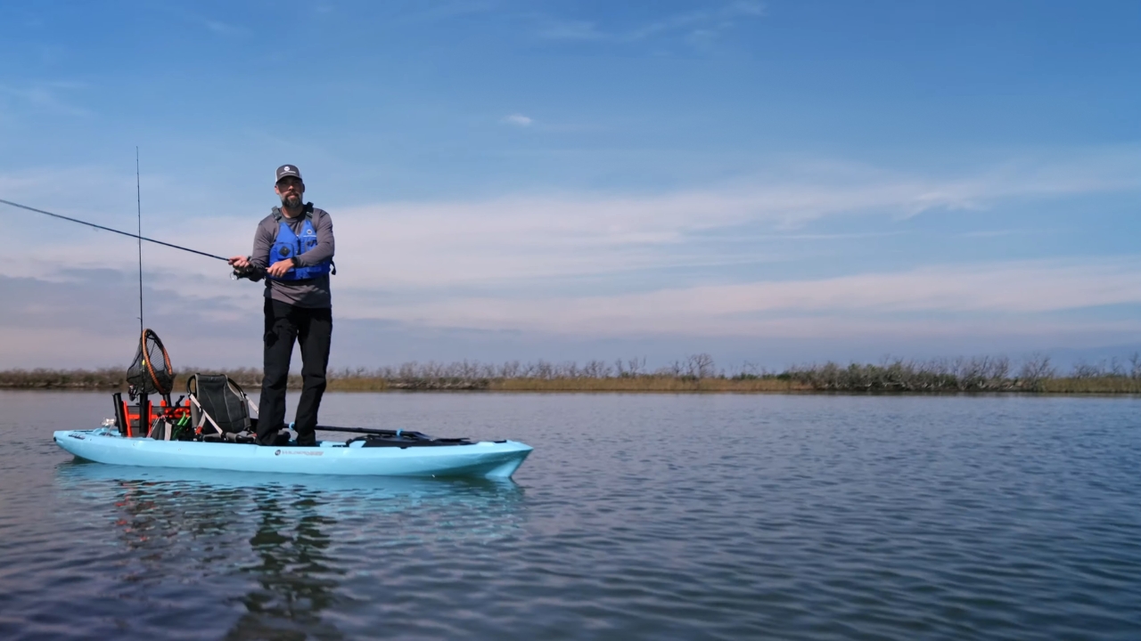 Angler standing on a blue fishing kayak in calm open water